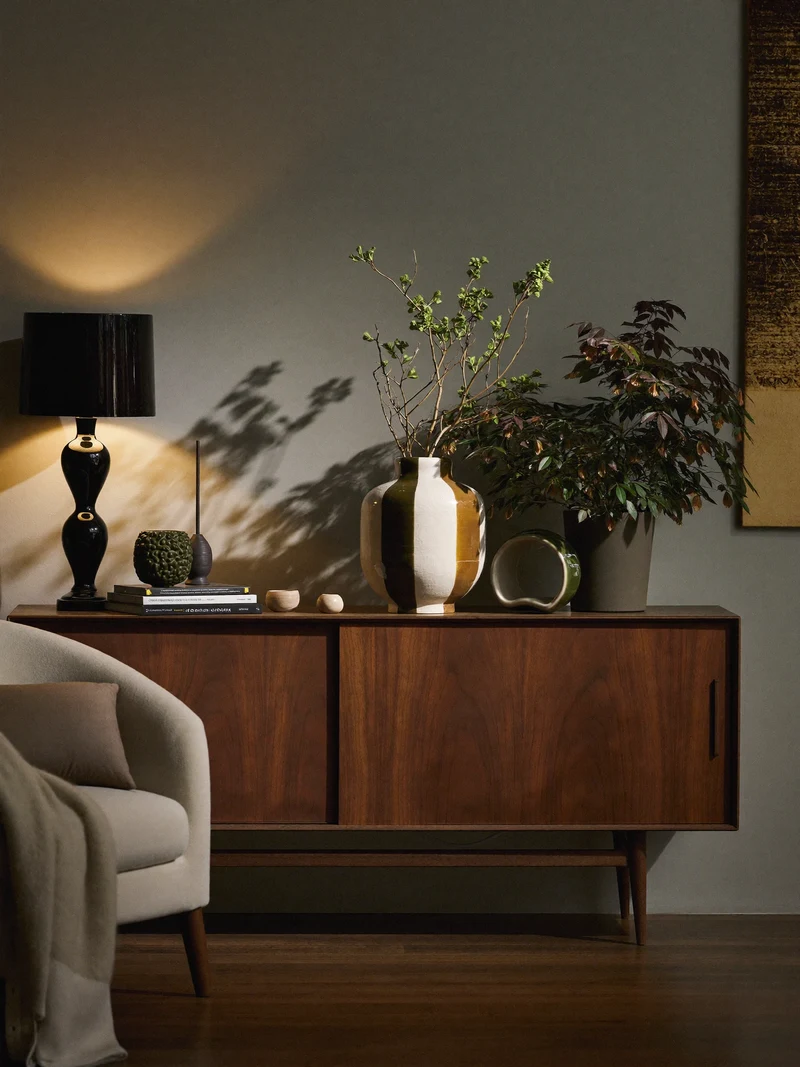 Illustration: Wohnzimmer am Abend mit warmem Lampenlicht und Sideboard